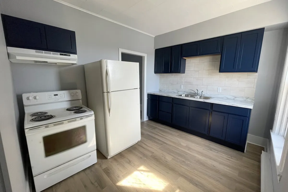 A kitchen with navy shaker cabinets, a white stove and fridge, and a tiled backsplash.