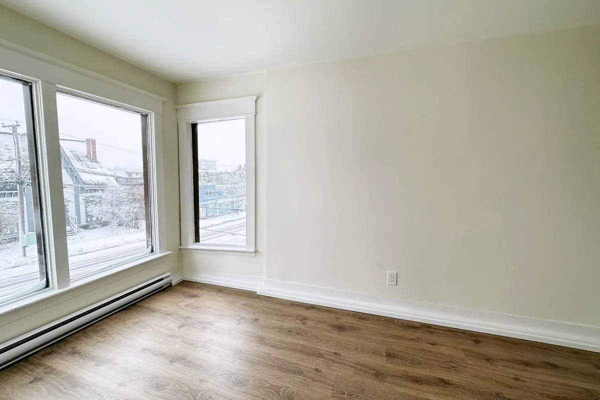 A bright empty front room with new plank floors, white walls and two large windows.