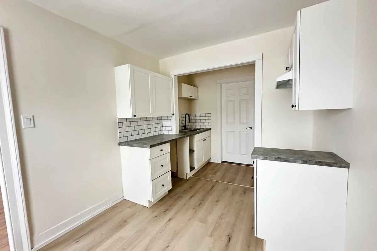 A small kitchen with white cabinets, subway tile, grey counters and plank floors.